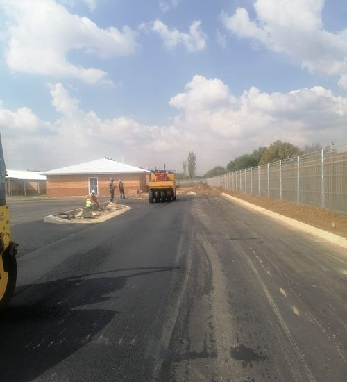 Mothetho Civils crew tarring an industrial yard in Gauteng — yellow roller, workers in high-visibility vests, fresh black asphalt and big Highveld sky